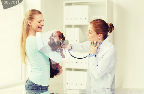 Image of happy woman with dog and doctor at vet clinic