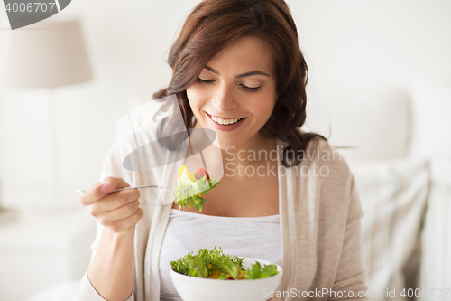 Image of smiling young woman eating salad at home