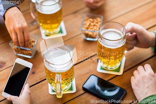 Image of close up of hands with smartphones and beer at bar