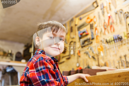 Image of happy little boy with wood plank at workshop