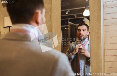 Image of man tying tie on at mirror in clothing store