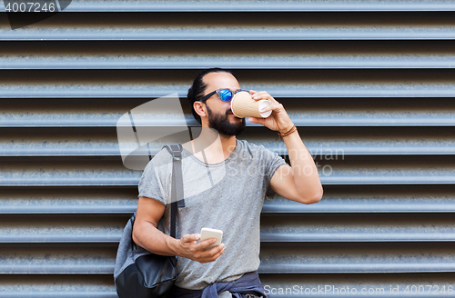 Image of man with smartphone drinking coffee on city street