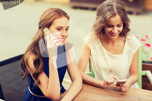 Image of happy young women with smartphones at outdoor cafe