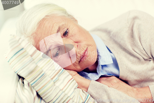 Image of sad senior woman lying on pillow at home