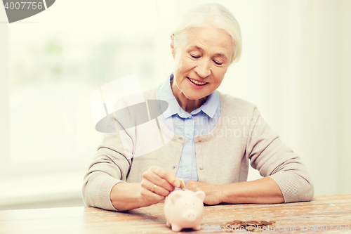 Image of senior woman putting money to piggy bank at home