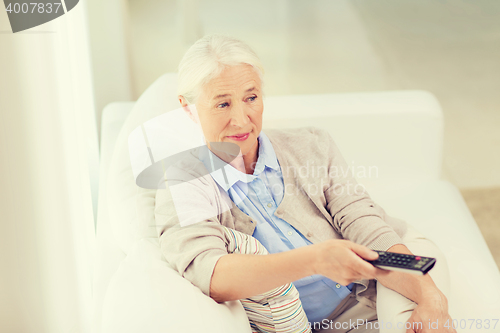 Image of senior woman with remote watching tv at home