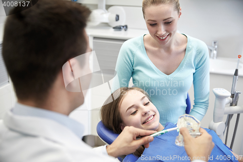 Image of happy dentist showing toothbrush to patient girl