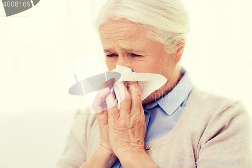 Image of sick senior woman blowing nose to paper napkin
