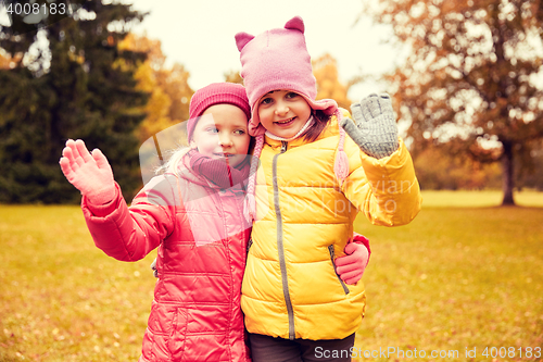 Image of two happy little girls waving hand in autumn park