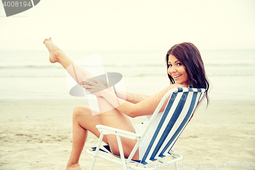 Image of smiling young woman sunbathing in lounge on beach