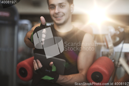 Image of young man with tablet pc showing thumbs up in gym