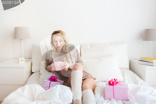 Image of happy young woman with gift boxes in bed at home