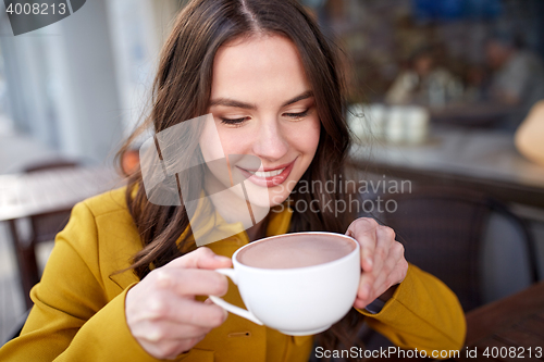 Image of happy woman drinking cocoa at city street cafe