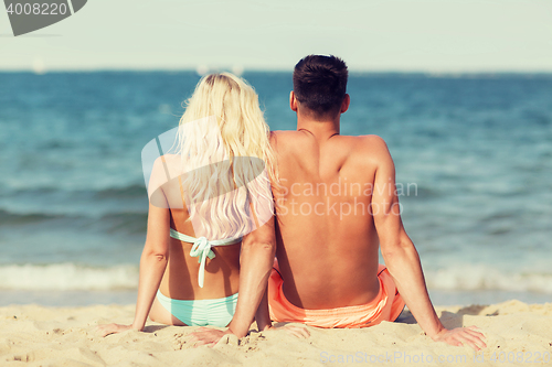 Image of happy couple in swimwear sitting on summer beach