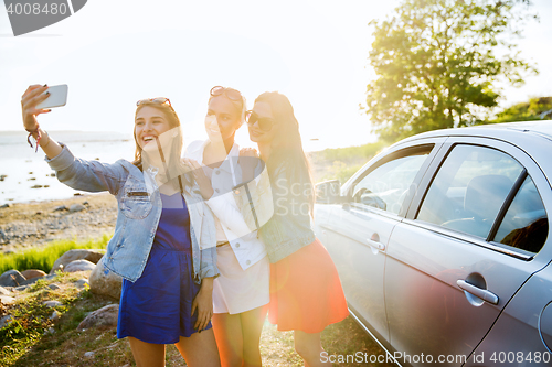 Image of happy women taking selfie near car at seaside