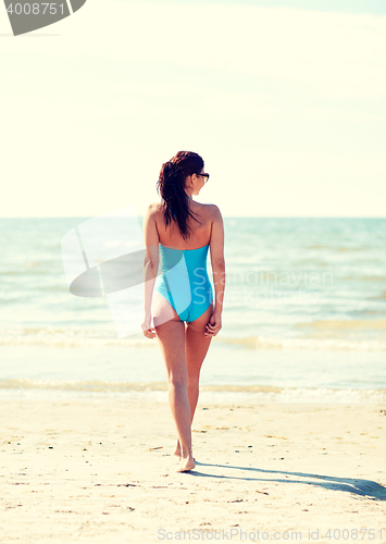 Image of young woman in swimsuit walking on beach