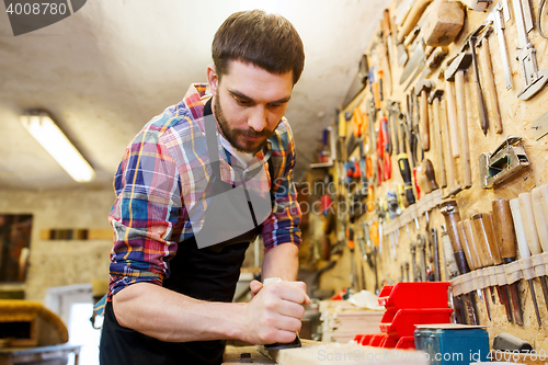 Image of carpenter working with plane and wood at workshop