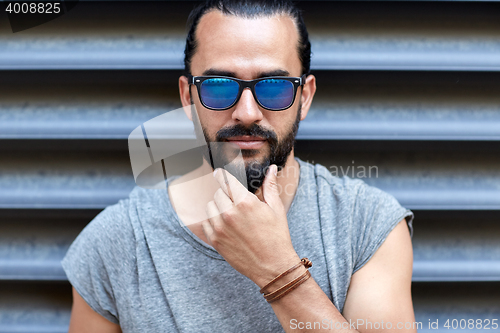 Image of man in sunglasses touching beard on city street