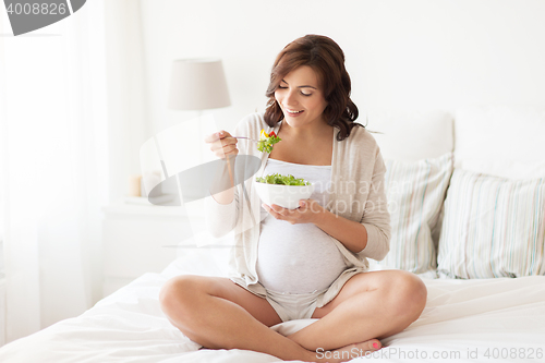 Image of happy pregnant woman eating salad at home