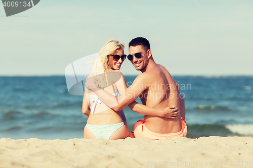 Image of happy couple in swimwear sitting on summer beach