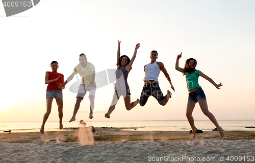 Image of smiling friends dancing and jumping on beach