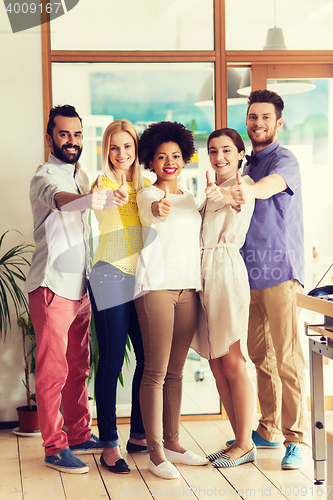 Image of happy creative team showing thumbs up in office