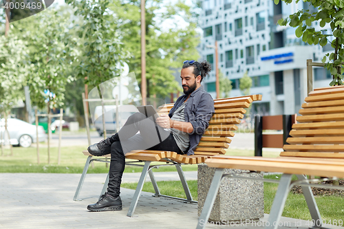 Image of man with tablet pc sitting on city street bench