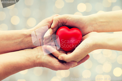 Image of senior and young woman hands holding red heart