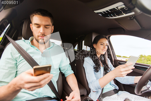 Image of man and woman with smartphones driving in car