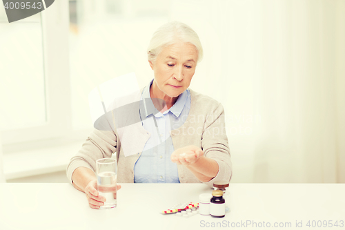 Image of senior woman with water and medicine at home