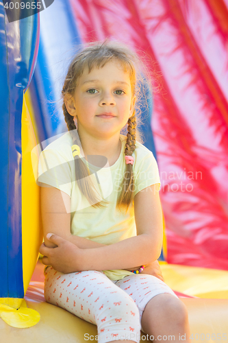 Image of Five-year girl naprygalis on a large inflatable trampoline sat down to rest