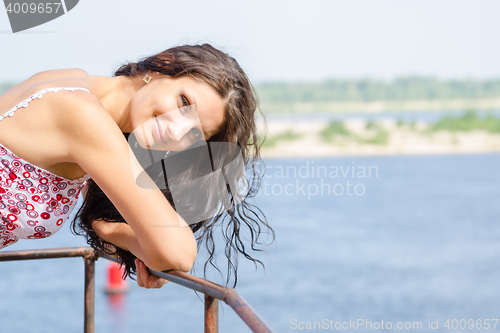 Image of Young girl in high spirits leaned on the old metal railings on the background of the river