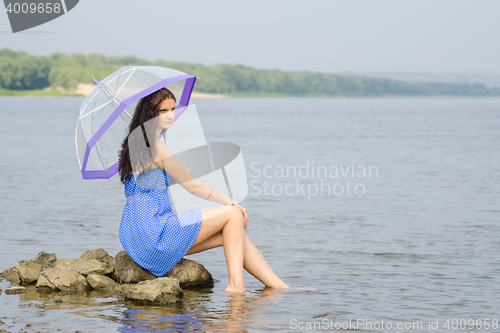 Image of Lonely sad young woman with an umbrella sits on a rock by the river