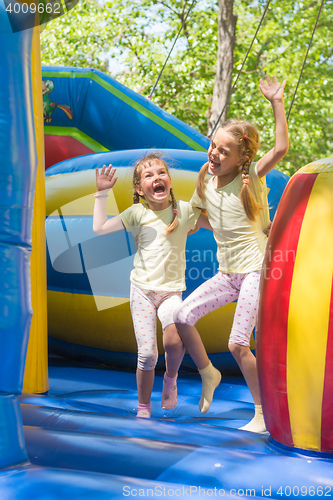 Image of Two girls grimacing happily jumping on an inflatable trampoline