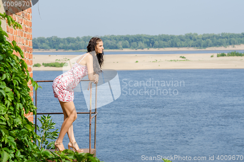 Image of Young brunette girl is standing on the balcony of the old against the backdrop of the river and looking thoughtfully into the distance