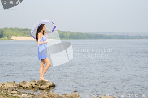Image of Lonely sad young girl with an umbrella stands on the bank of the river and looks into the distance