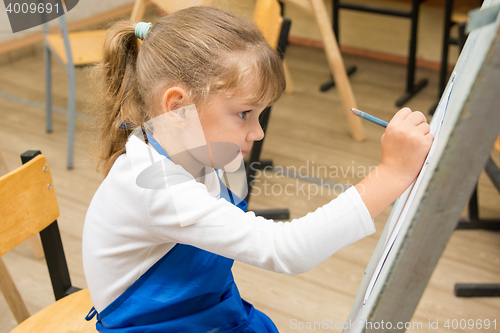 Image of Five-year girl paints on an easel in the drawing lesson