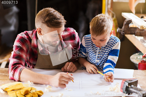 Image of happy father and son with blueprint at workshop