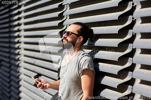 Image of man with earphones and smartphone on city street