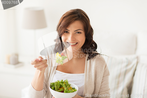 Image of smiling young woman eating salad at home