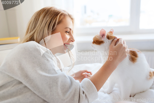 Image of happy young woman with cat in bed at home