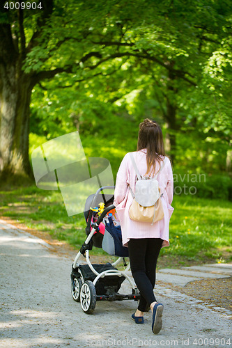 Image of Happy mother walking with baby stroller in park