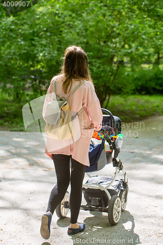 Image of Happy mother walking with baby stroller in park