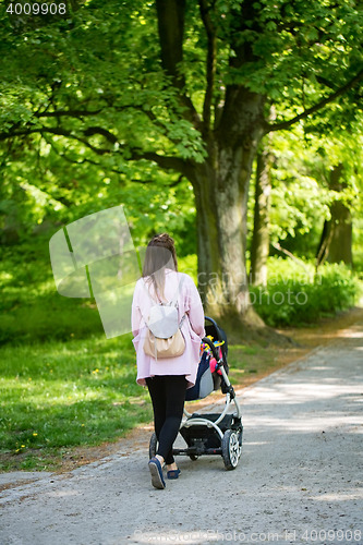 Image of Happy mother walking with baby stroller in park