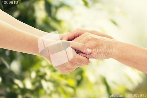 Image of close up of senior and young woman holding hands