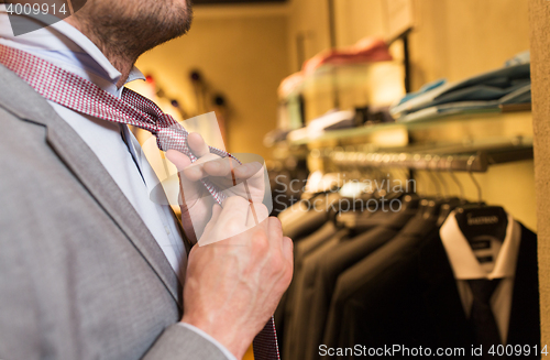 Image of close up of man tying tie at clothing store mirror