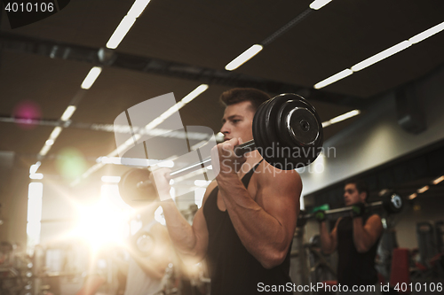 Image of young men flexing muscles with barbells in gym