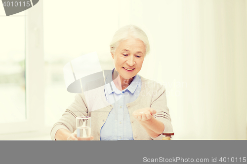 Image of happy senior woman with water and medicine at home