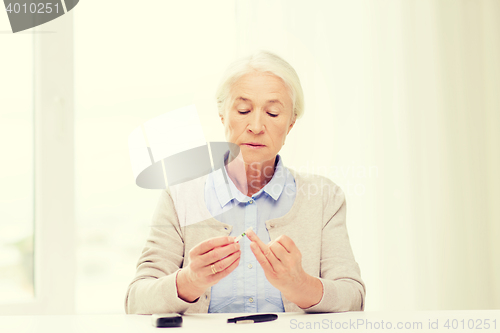 Image of senior woman with glucometer checking blood sugar