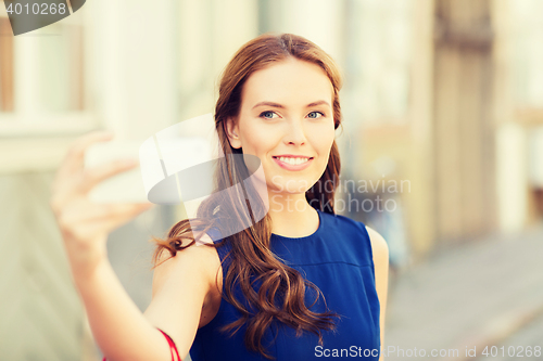 Image of happy woman taking selfie with smartphone in city